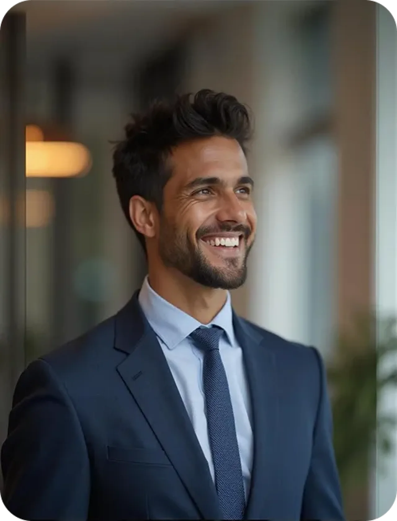 Smiling professional man in a navy suit and tie standing in a contemporary office setting, exuding confidence and approachability.