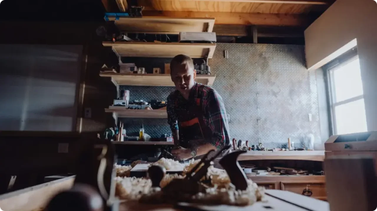 A man diligently crafts a woodworking project in his well-equipped workshop, surrounded by tools and materials.