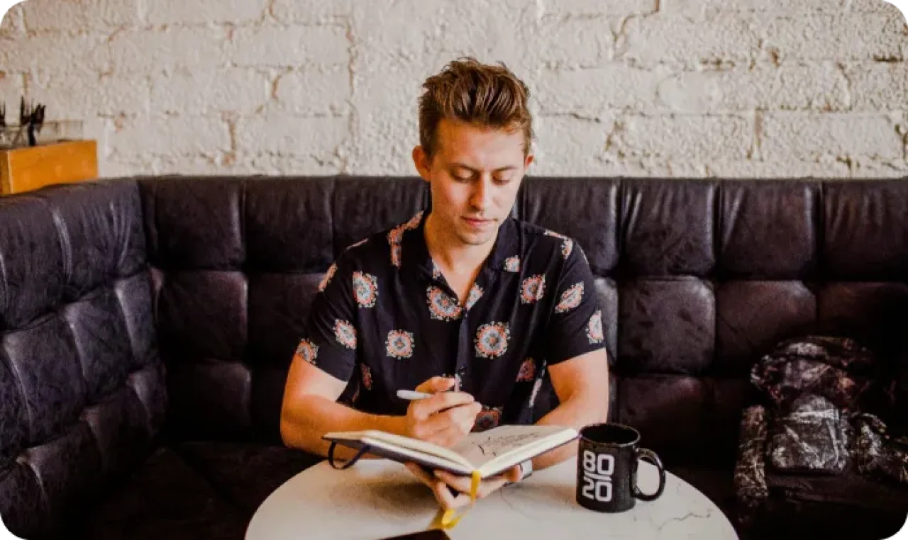 A man writing something in his notebook at a cafe.