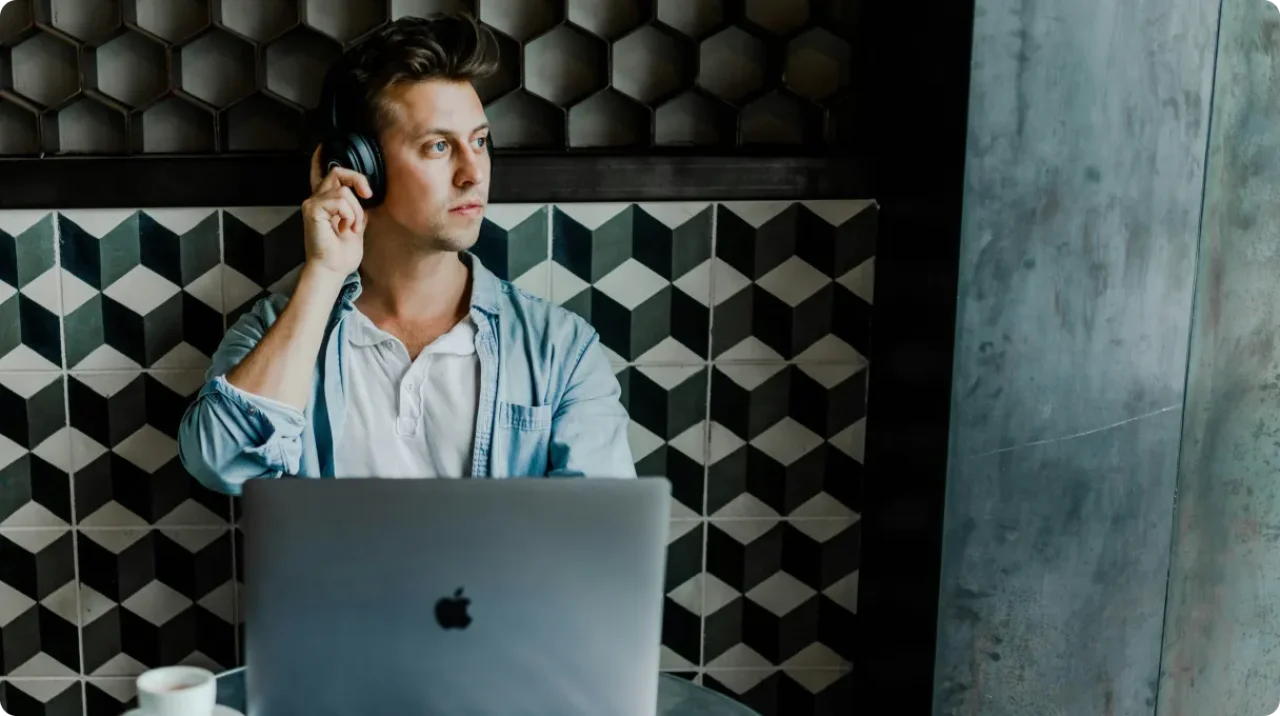 A man sitting with laptop, and earphones - looking slightly into window
