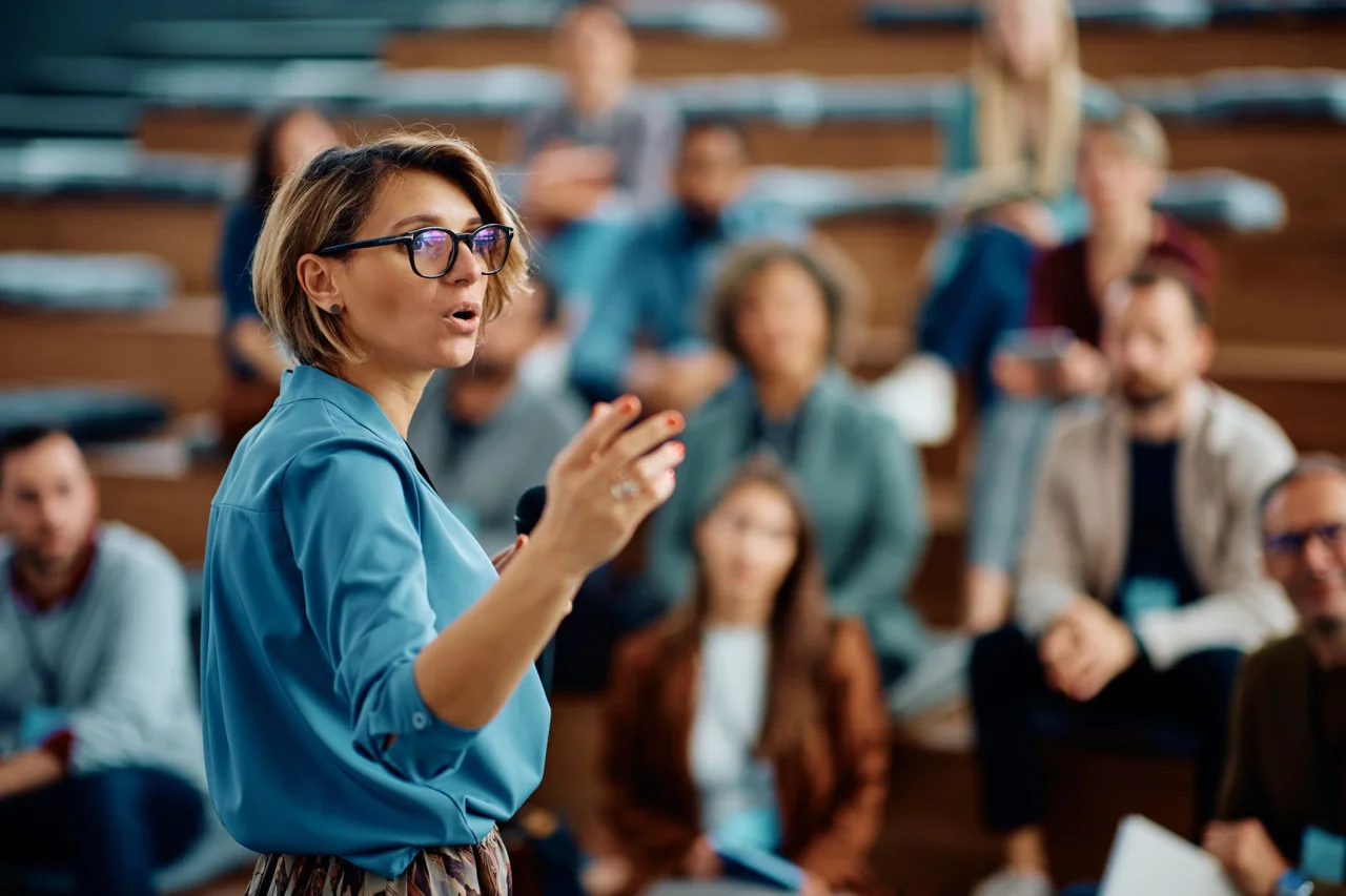 Woman giving a presentation in front of a seated audience during a business seminar or workshop.