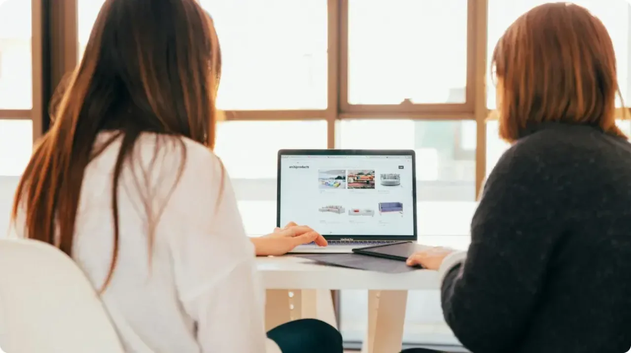 Two Women Collaborating On Laptop At Desk