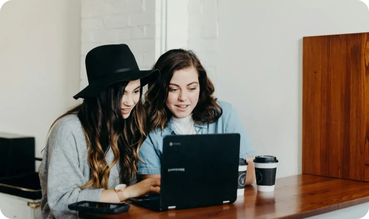 Two Women Working Together On Laptop At Cafe