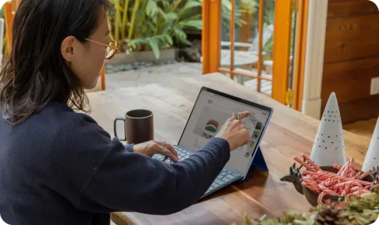 Woman using a touchscreen laptop or tablet at a wooden table in a cozy home workspace