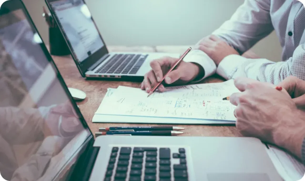 Two professionals reviewing financial documents and business plans with laptops and notes during a meeting.