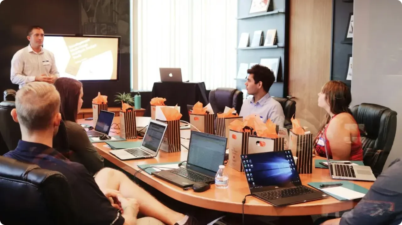 Man standing in front of people sitting beside table with laptop computers