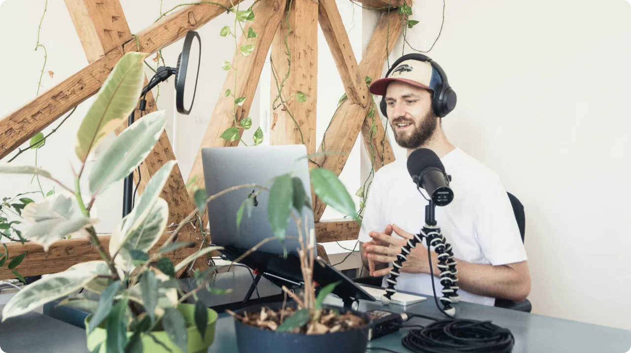 Man recording a podcast or virtual meeting at a remote workspace with professional microphone, laptop, and headphones.
