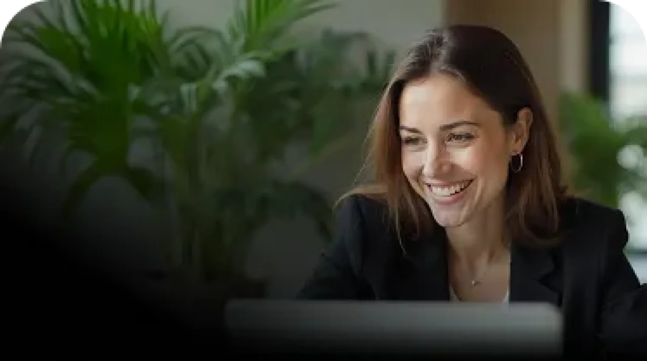 Smiling professional woman in a blazer participating in a video call from a modern office with indoor plants